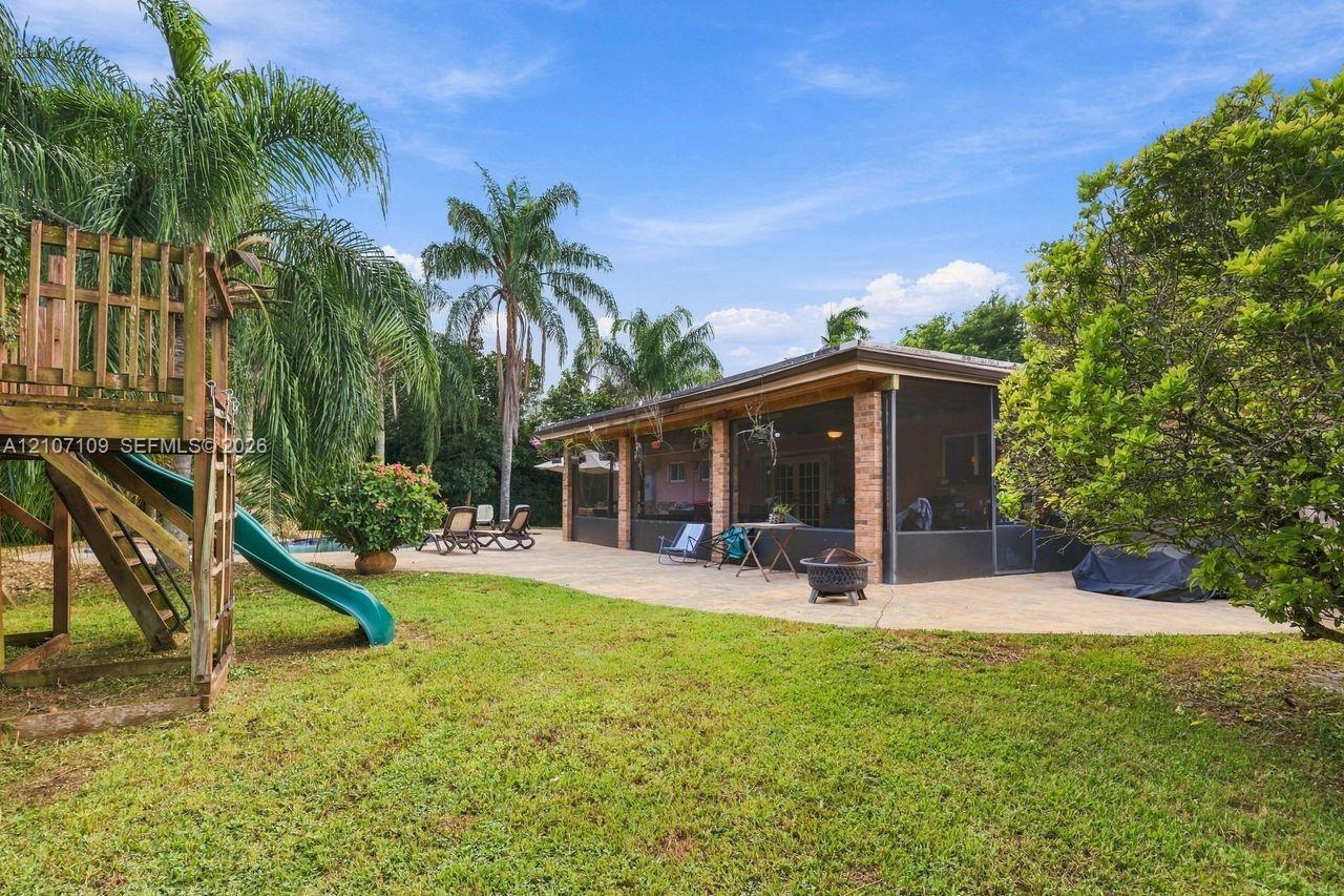 Backyard featuring a screened-in patio, expansive concrete hardscaping, brick exterior accents, and mature landscaping