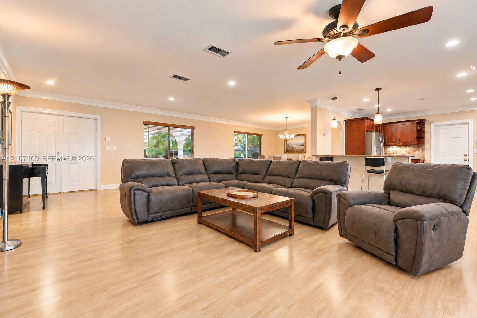Open-concept area featuring wood-finish flooring, recessed lighting, a ceiling fan with integrated light fixture, and crown molding