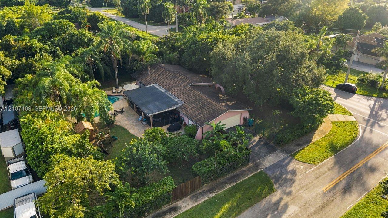 Aerial perspective featuring a multi-pitched roof, attached garage, paved driveway, screened-in patio, and swimming pool within a landscaped lot
