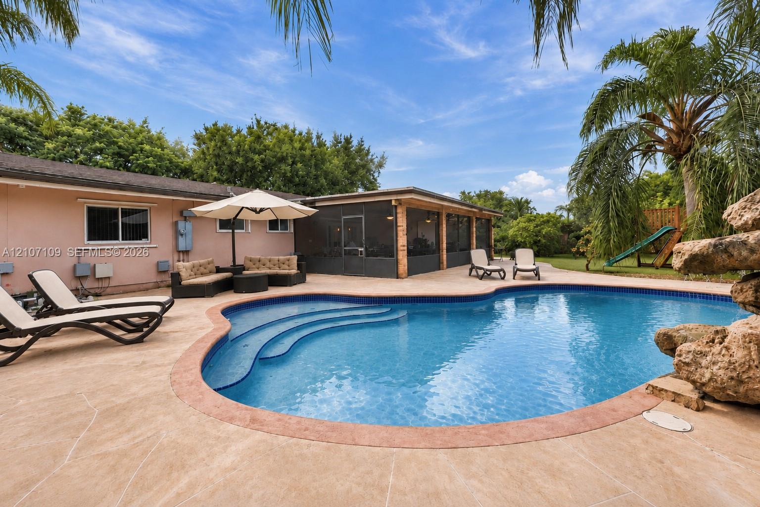In-ground swimming pool featuring built-in stairs, decorative stone accent, concrete paver decking, and a screened-in lanai In-ground swimming pool featuring built-in stairs, decorative stone accent, concrete paver decking, and a screened-in lanai
