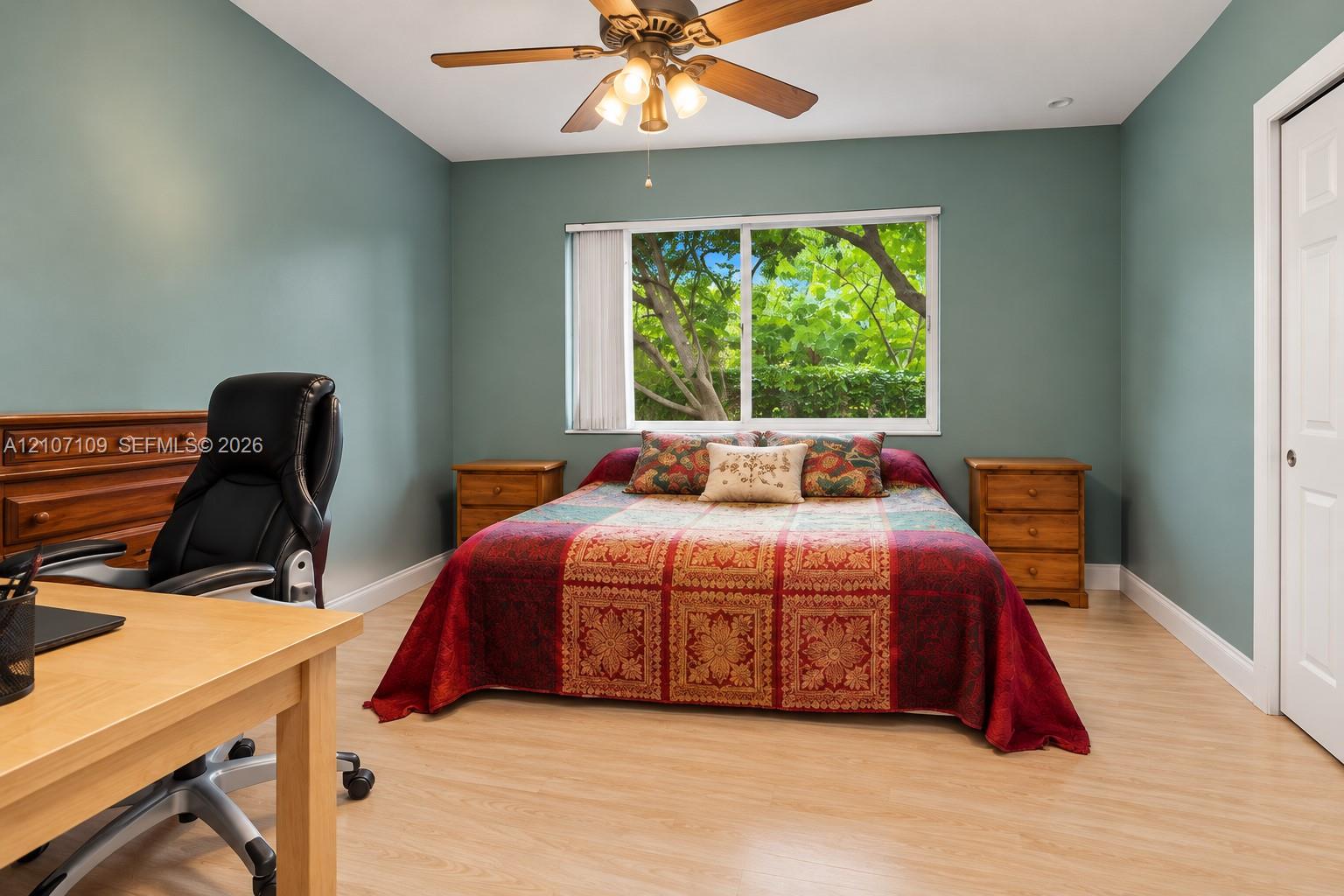 Light-filled room featuring wood-finish flooring, a ceiling fan with integrated lighting, and a window with exterior greenery