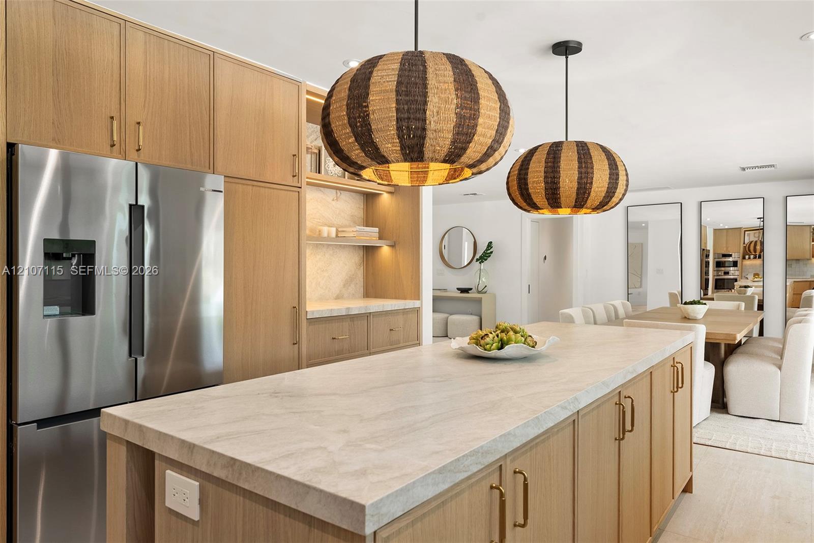 Kitchen featuring light-tone wood cabinetry, stone countertops, stainless steel refrigerator, and two hanging woven pendant lights