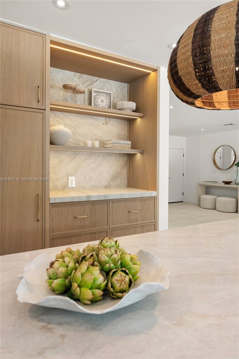 Built-in wood-finish cabinetry featuring integrated recessed lighting, stone-surface countertop, open shelving, and brushed brass hardware