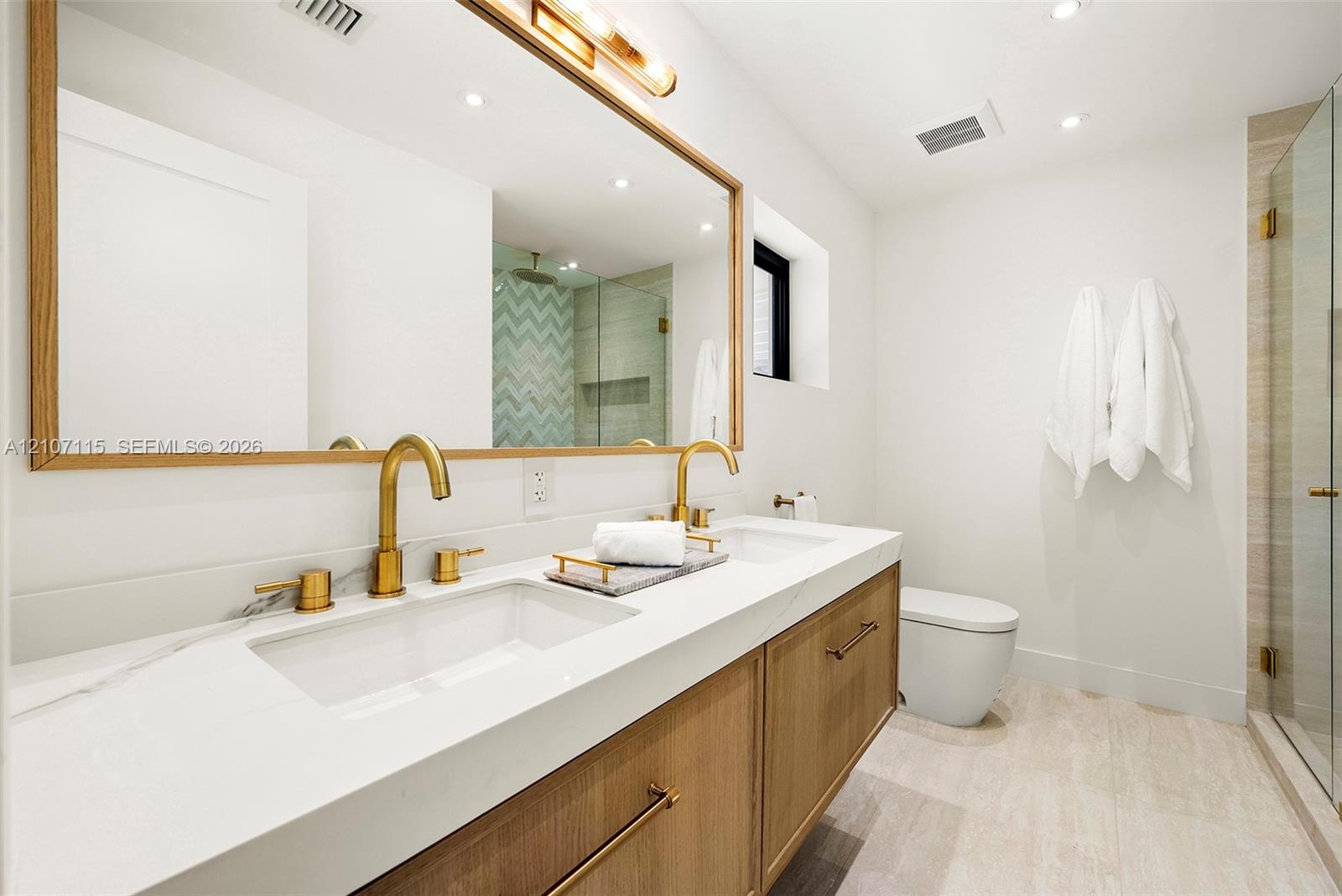 In suite Bathroom Double vanity featuring wood-finish cabinetry, white countertop with dual undermount sinks, gold-tone fixtures, and a large wood-framed mirror