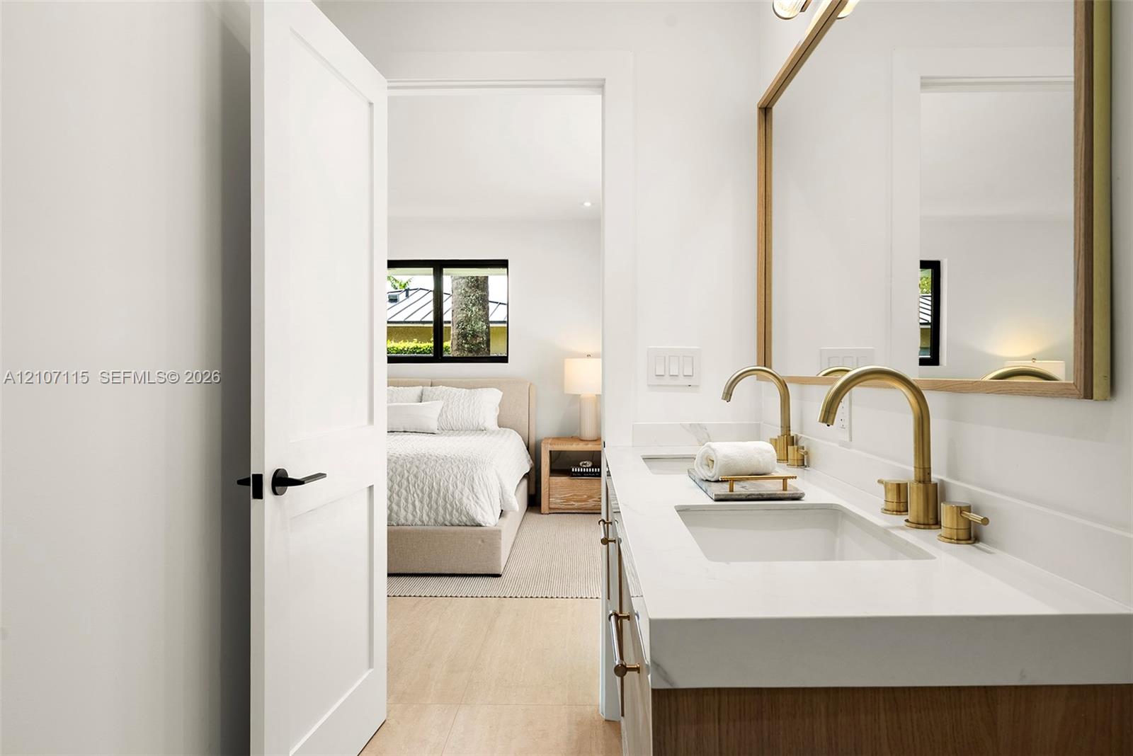 Dual-sink vanity with quartz countertop, brass-toned fixtures, wood-finish cabinetry, and a large framed mirror