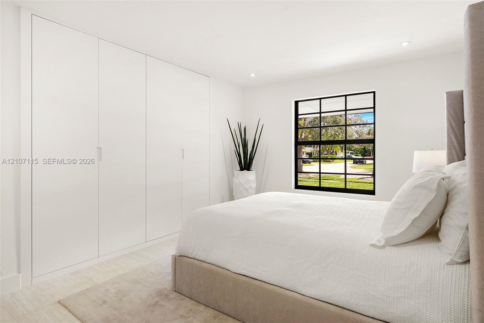 Bedroom 3 Full-wall built-in cabinetry with flush-panel doors, grid-pattern window with matte black frame, recessed ceiling lighting, and neutral stone-finish flooring