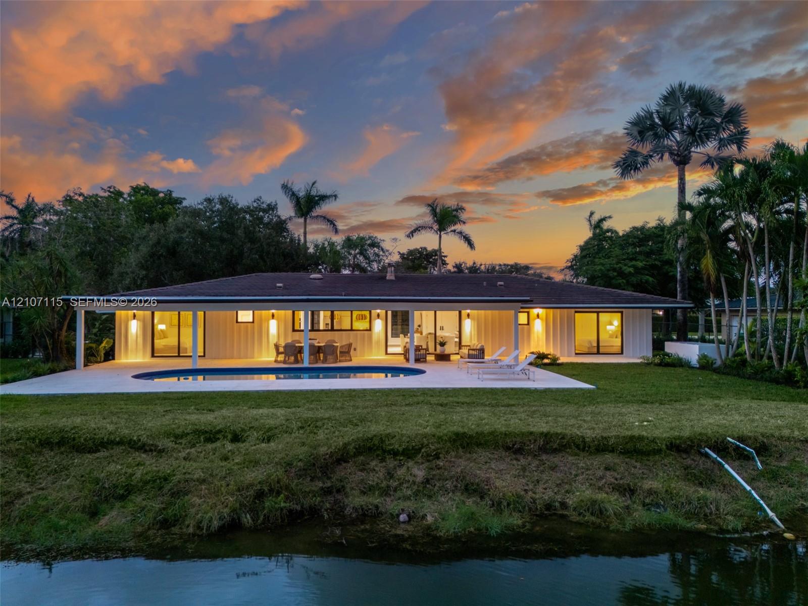 Waterfront residence featuring a covered patio, swimming pool, expansive lawn, and architectural vertical siding