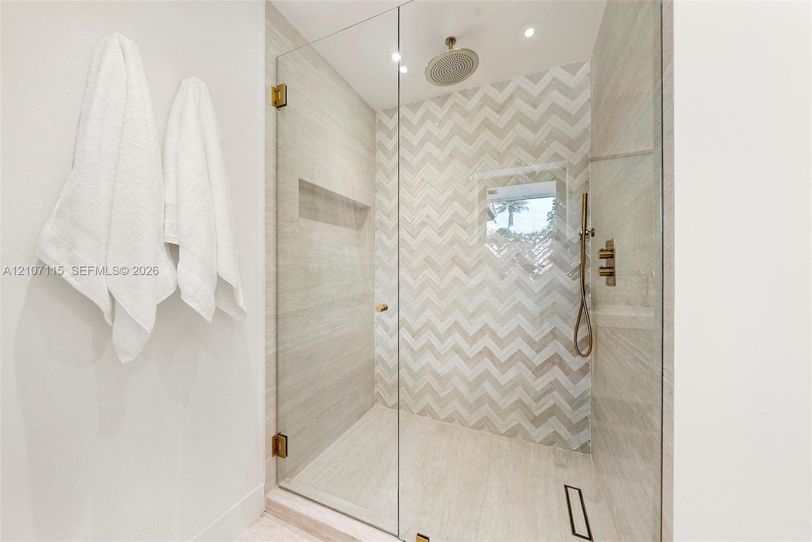 Walk-in shower featuring a chevron-patterned tile accent wall, glass enclosure, recessed wall niche, rainfall showerhead, and a handheld fixture