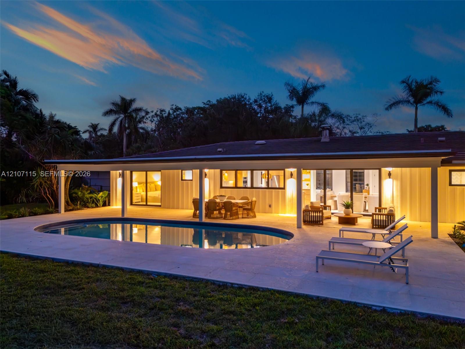 Single-story exterior featuring vertical siding, an expansive covered patio, an oval-shaped pool, and mature palm trees