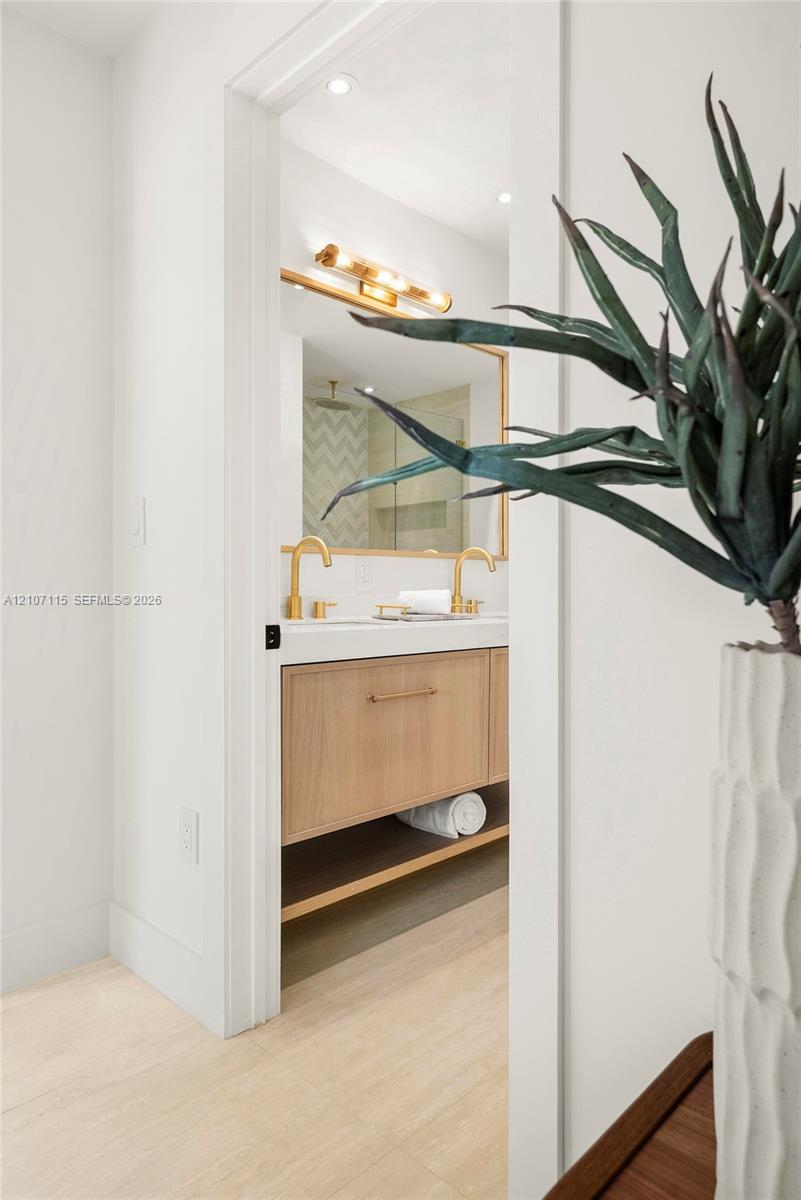 Floating vanity featuring wood-finish cabinetry, a white countertop with integrated double sinks, metallic hardware, and a minimalist-style vanity light fixture