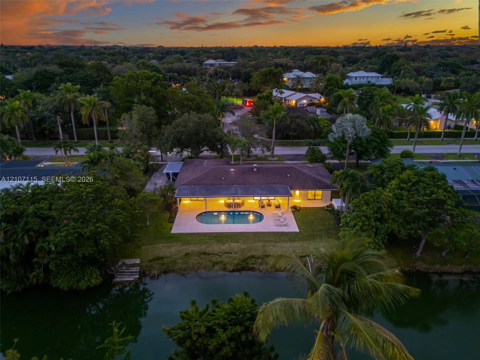 Aerial perspective of a waterfront property featuring a paved rear patio, in-ground pool, covered veranda, and mature landscaping Aerial perspective of a waterfront property featuring a paved rear patio, in-ground pool, covered veranda, and mature landscaping