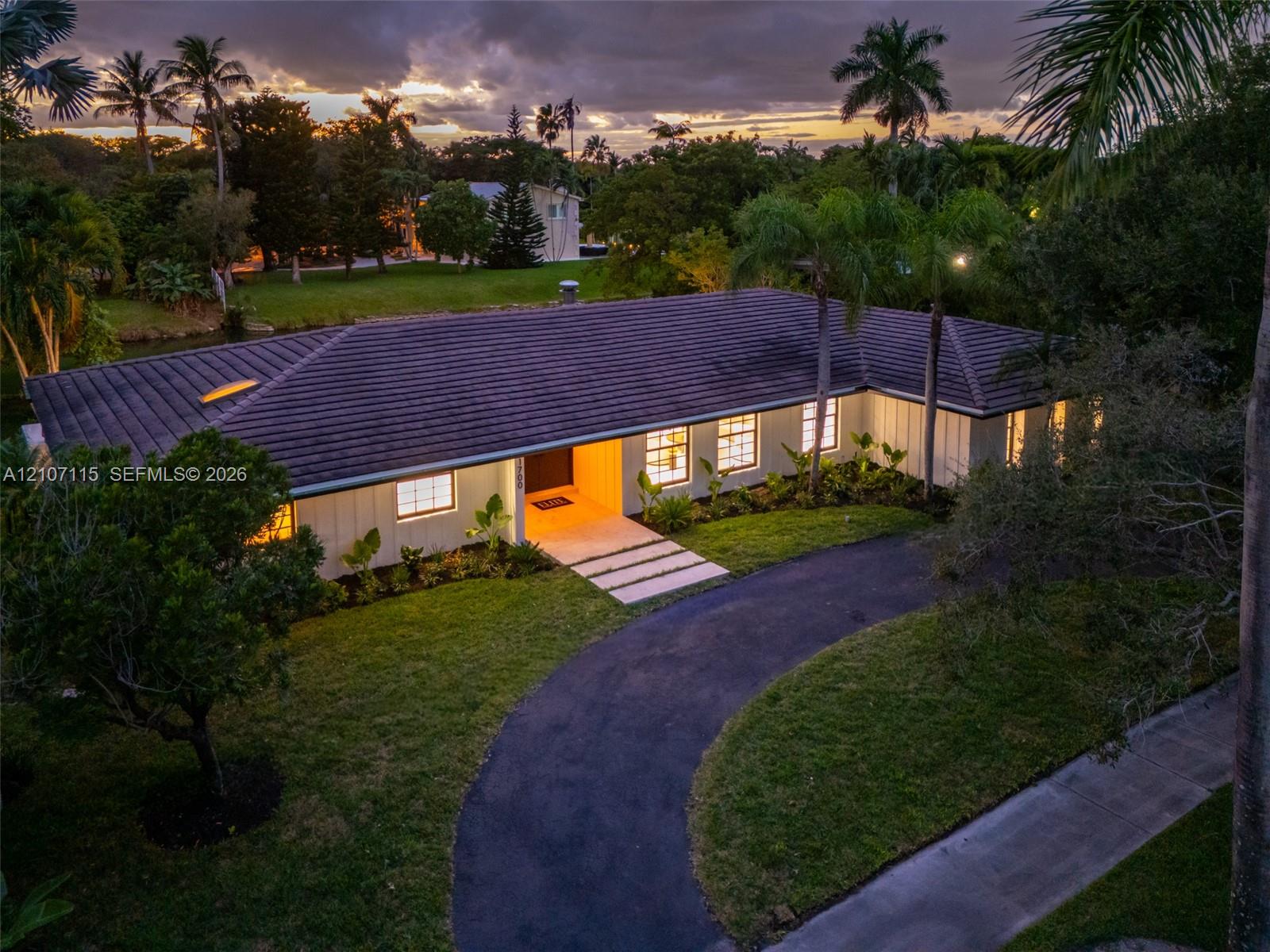 Single-story residence featuring a tile roof, board-and-batten siding, a curved asphalt driveway, and expansive lawn landscaping