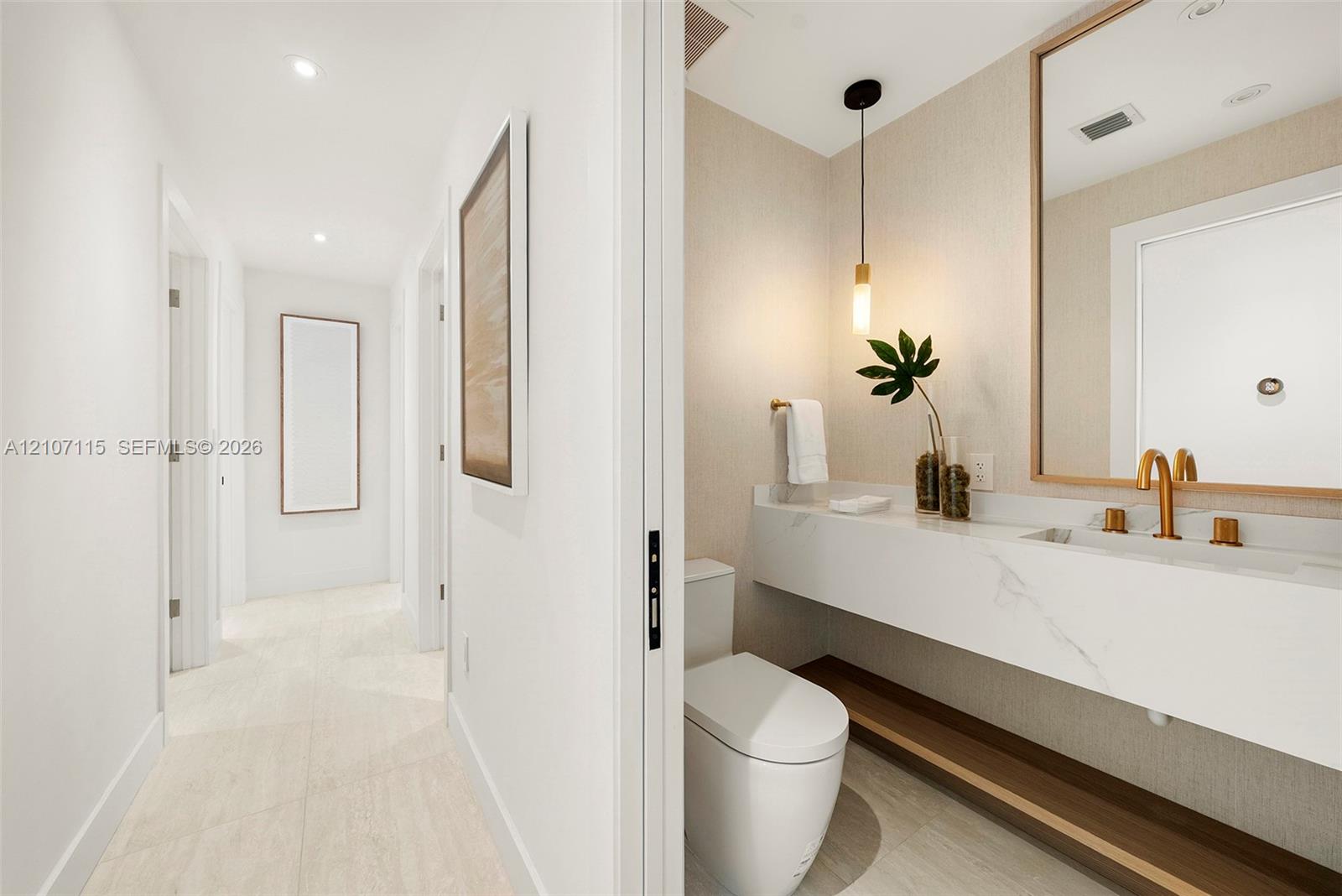 Powder room Floating vanity with stone-surfaced countertop, integrated rectangular sink, brass-finish fixtures, textured wall covering, and pendant lighting