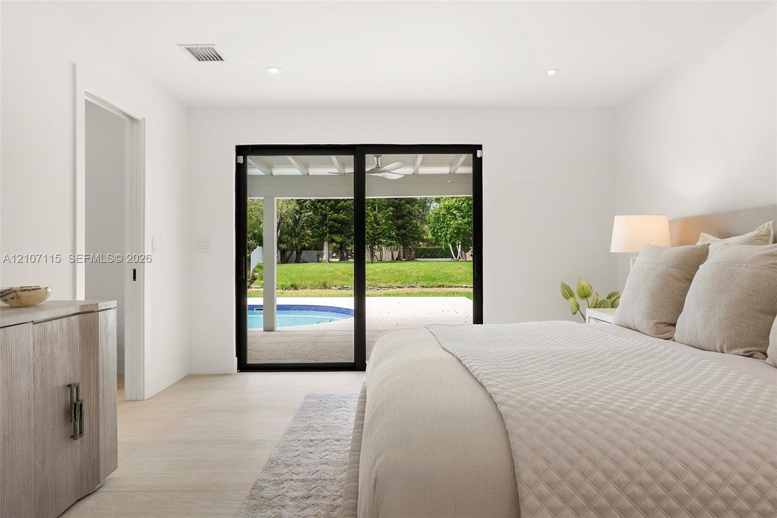 Light-filled interior featuring sliding glass doors with black frames, neutral stone-finish flooring, and recessed lighting