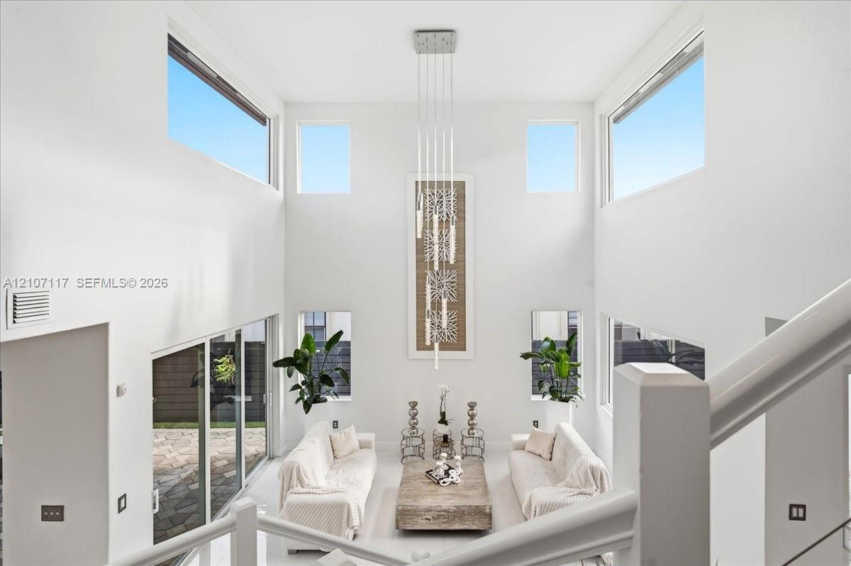 Double-height ceilings, expansive window configuration, multi-level glass slider access to exterior patio, and tiered contemporary pendant lighting