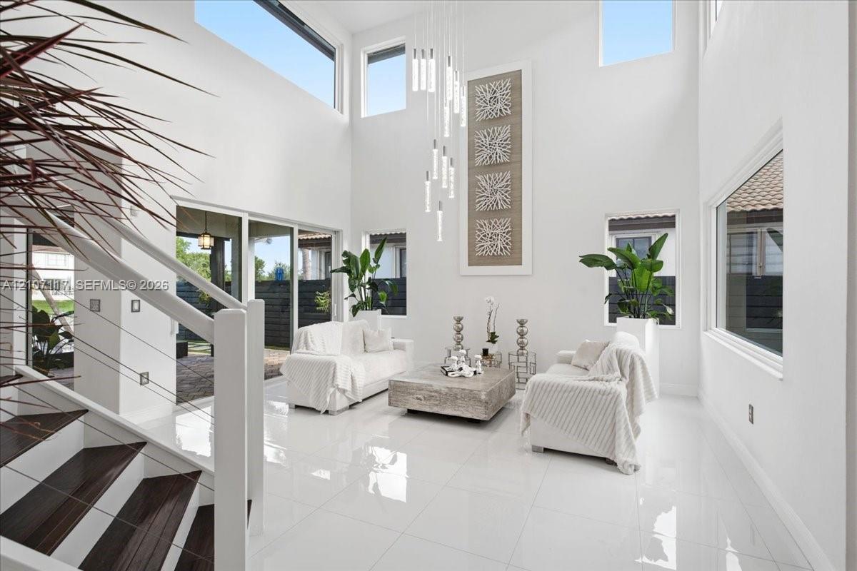 Double-height ceilings featuring tiered modern pendant lighting and multi-level windows, polished porcelain tile flooring, and a staircase with wood-finish treads and cable railing