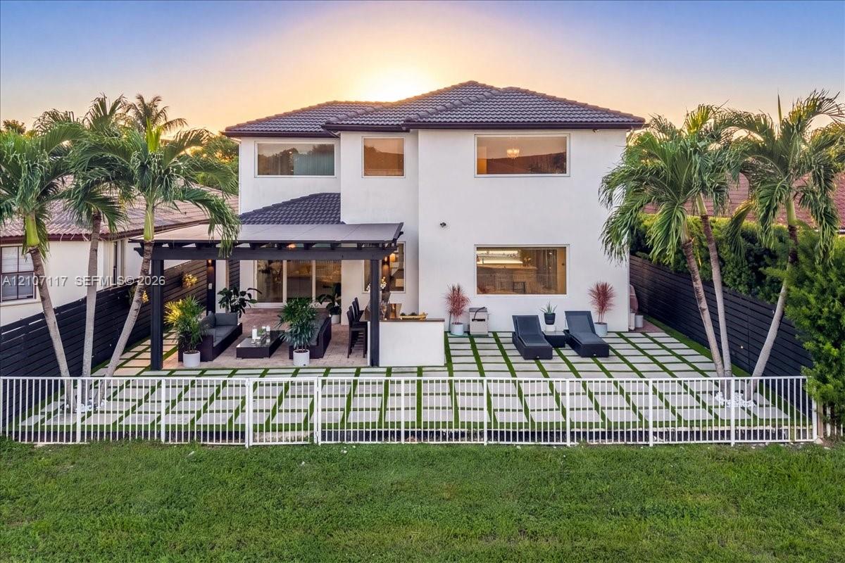 Two-story residence featuring a tile roof, an expansive paver patio with grass inserts, a covered pergola, and a white aluminum perimeter fence