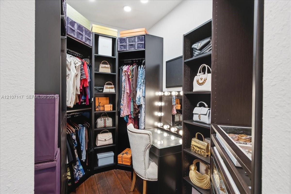 Custom dressing area featuring dark wood-finish cabinetry, built-in shelving, integrated vanity with glass countertop, and recessed ceiling lighting