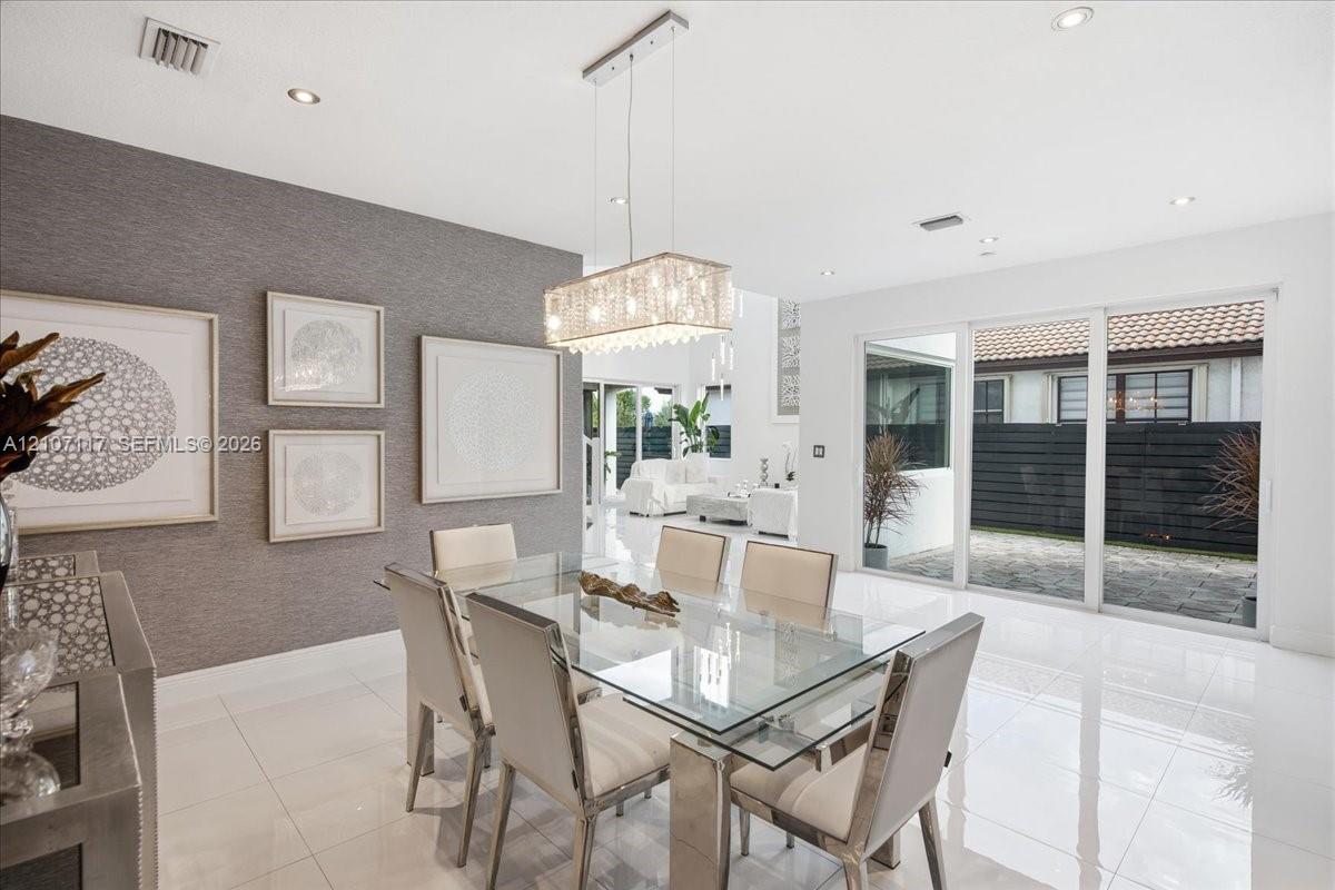 Dining area featuring large-format tile flooring, textured accent wall, rectangular tiered crystal chandelier, and oversized glass sliding doors