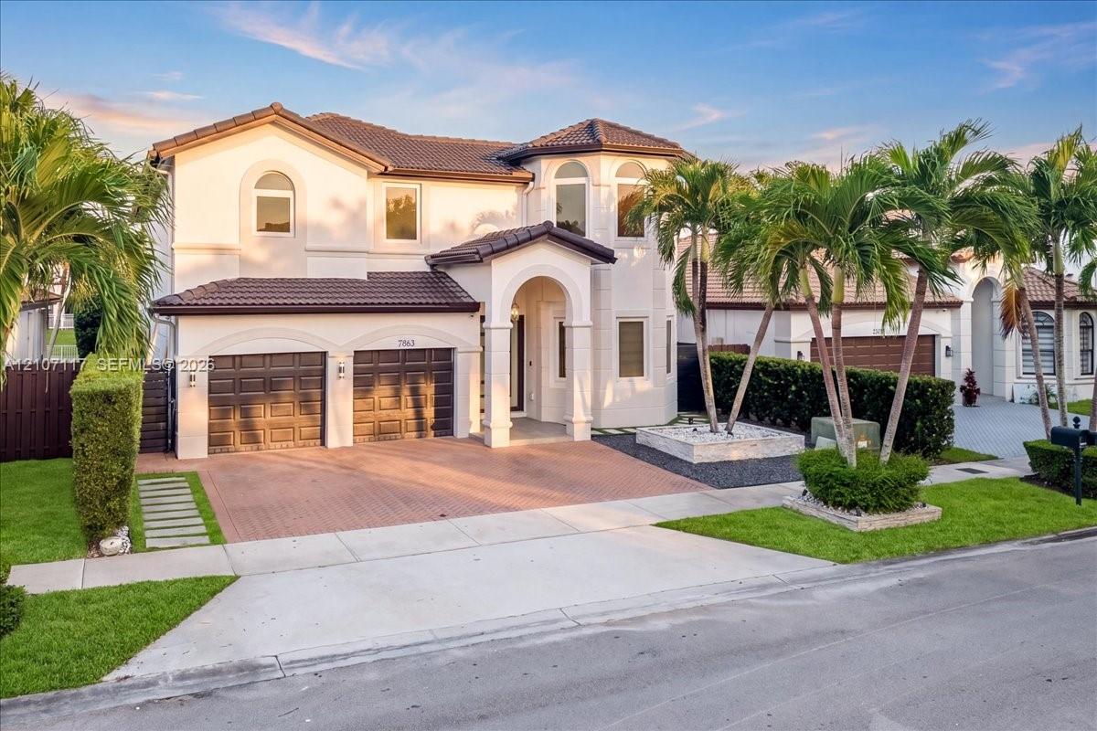 Two-story stucco exterior featuring a covered arched entryway, tiled roof, decorative masonry planter, and a multi-car garage with paneled doors