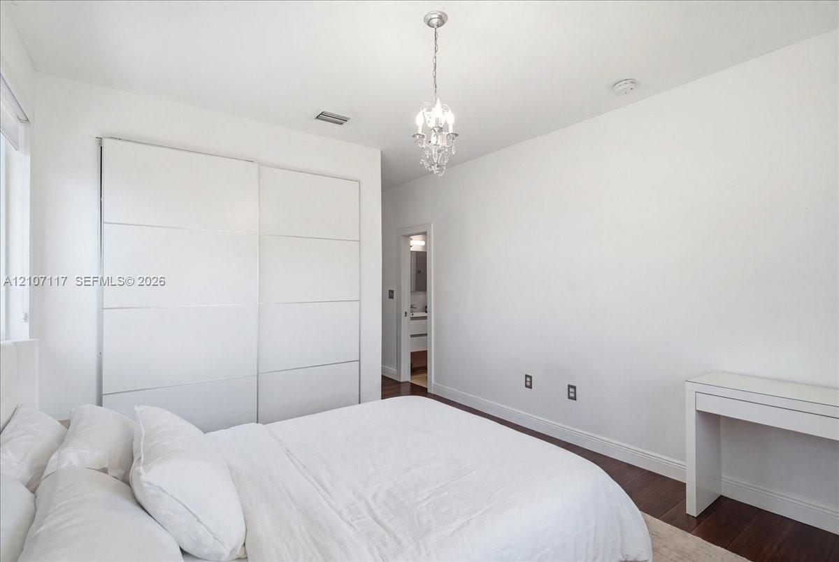 Room featuring dark wood-finish flooring, floor-to-ceiling built-in sliding door wardrobe, and a crystal chandelier