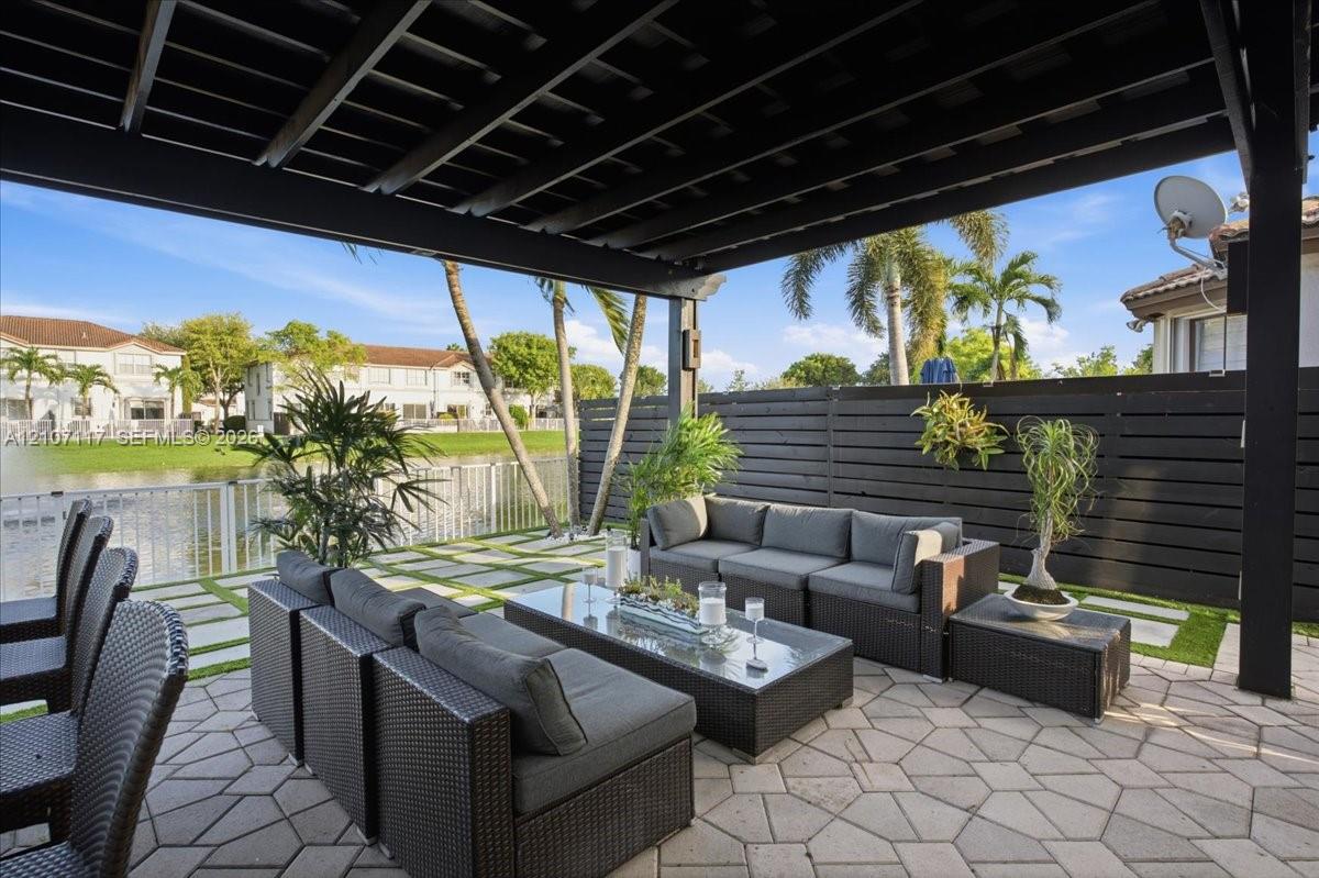 Covered patio featuring a black timber pergola, horizontal privacy fencing, concrete pavers with integrated turf, and water frontage