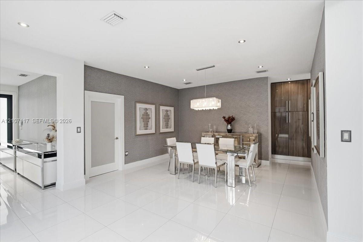 Open-concept interior featuring large-format polished tile flooring, textured wall coverings, a modern rectangular chandelier, and built-in full-height wood-finish cabinetry