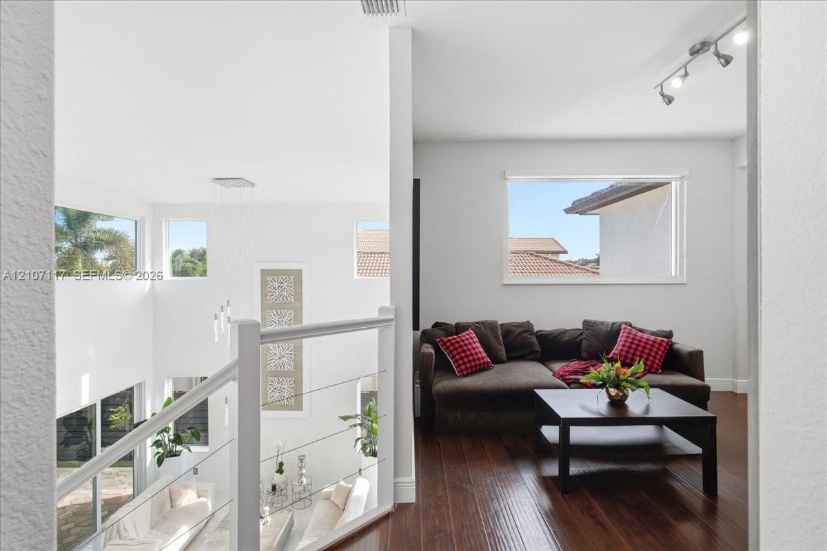 Open mezzanine featuring wood-finish flooring, metal cable railing, recessed track lighting, and multi-level window placements