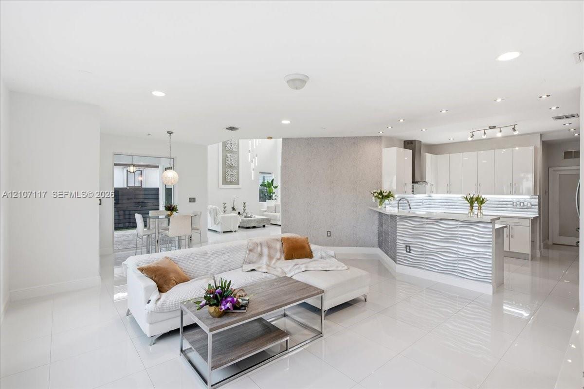 Open-concept interior featuring large-format tile flooring, high-gloss kitchen cabinetry, a textured stone feature wall, and a raised breakfast bar with horizontal wave-patterned paneling