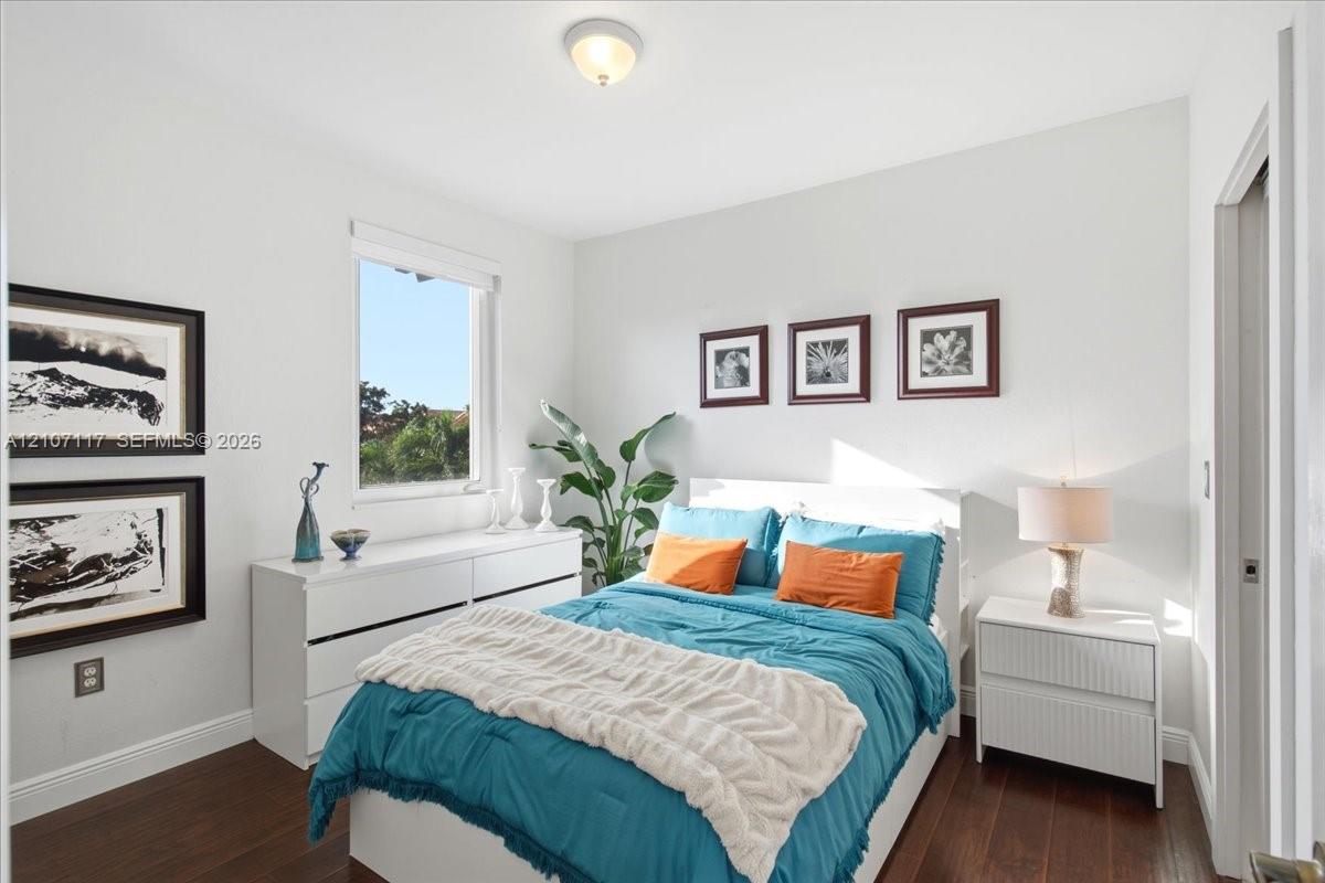 Bedroom interior featuring dark wood-finish flooring, neutral wall tones, a single-hung window, and a flush-mount ceiling light fixture