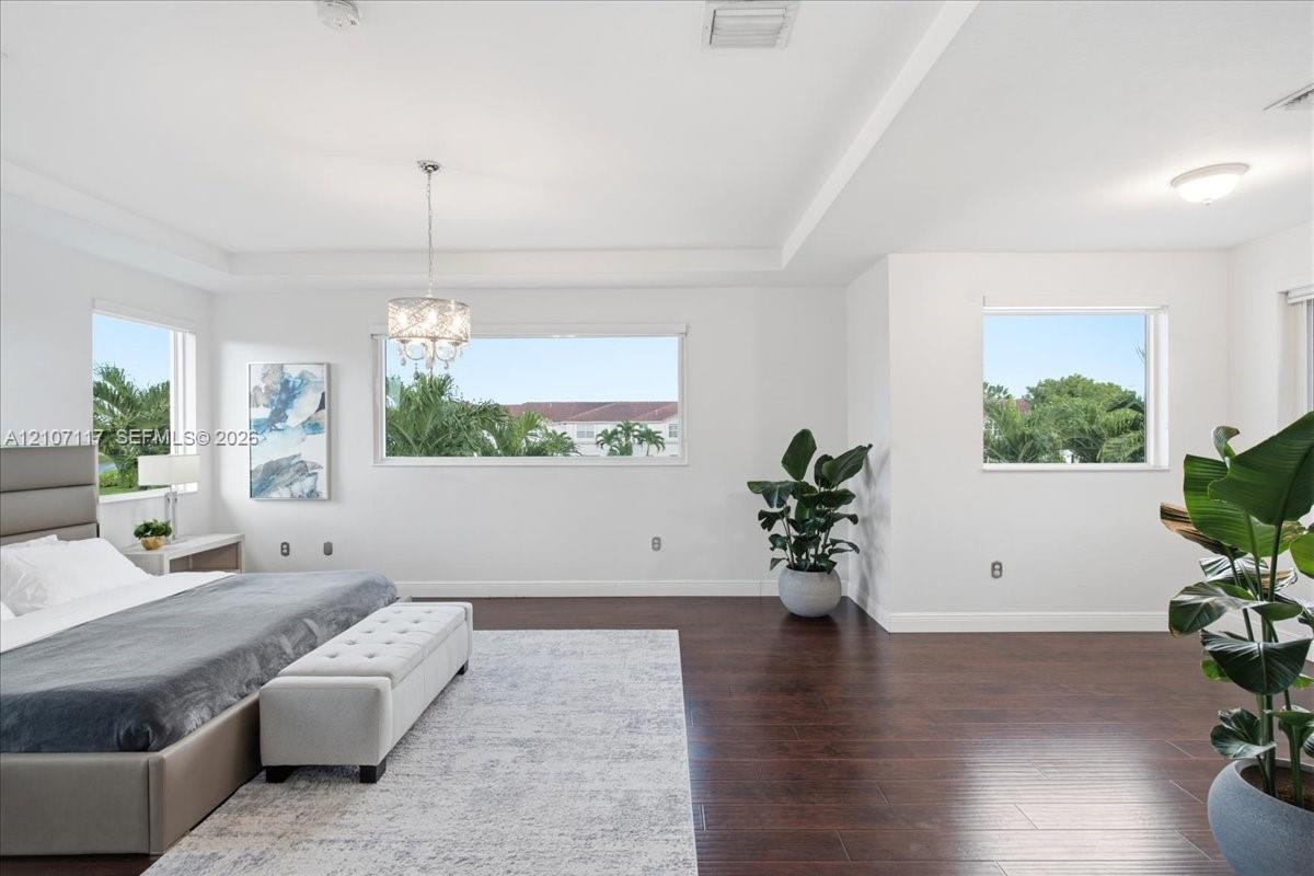 Spacious room featuring wood-finish flooring, recessed ceiling tray detailing, and a multi-tiered crystal chandelier
