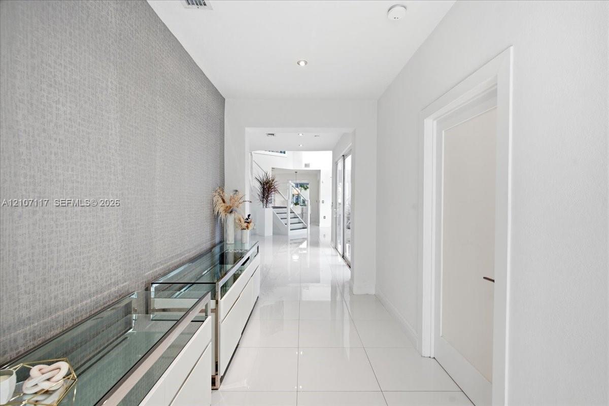 Hallway featuring polished white tile flooring, recessed lighting, and a textured grey accent wall