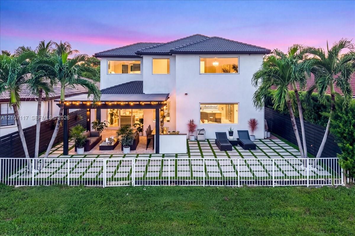 Two-story residence featuring a paved patio with turf grid patterns, a covered pergola, integrated outdoor cabinetry, and privacy fencing