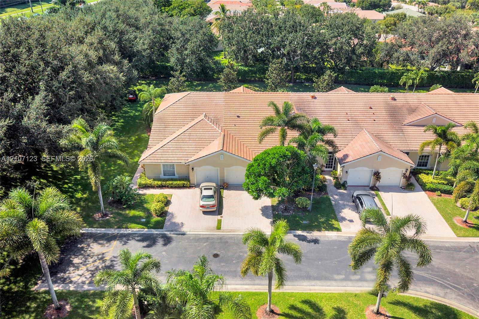 Multi-unit residence featuring a tile roof, paved driveways, integrated garages, and mature palm landscaping
