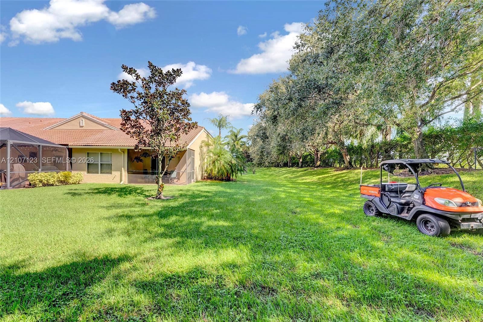 Expansive backyard featuring a manicured lawn, mature trees, tiled-roof exterior, and a screened-in patio