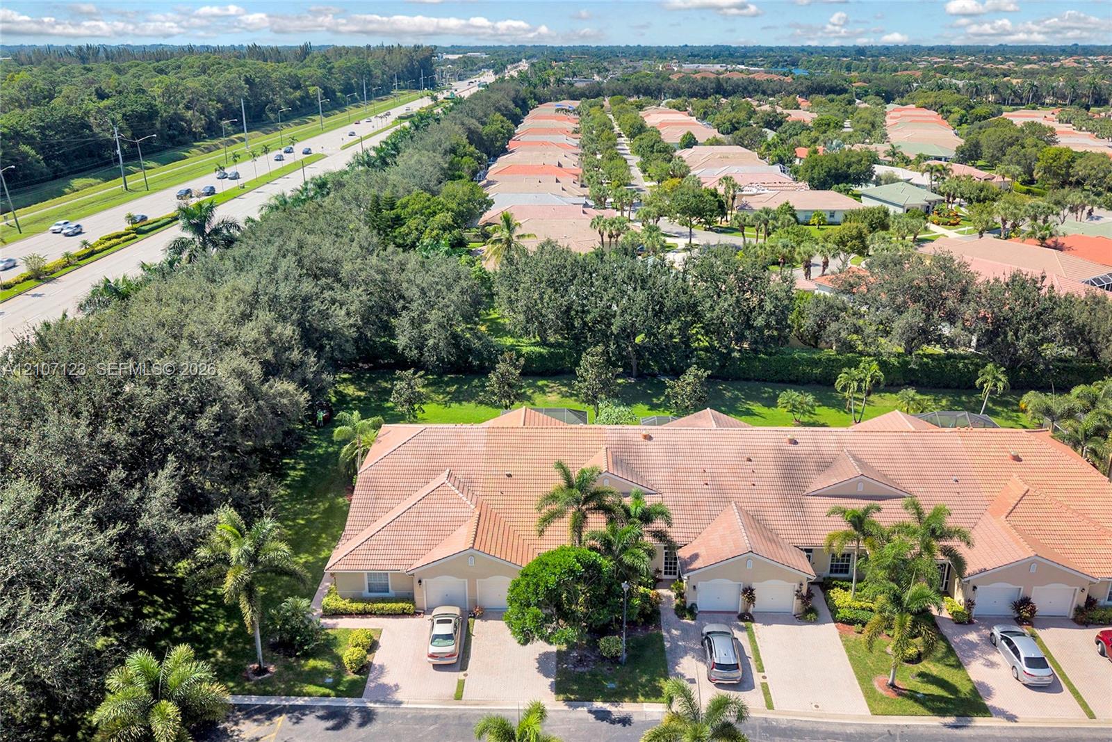 Aerial perspective of a multi-unit residential building featuring a tile roof, concrete driveways, and mature landscaping with palm trees