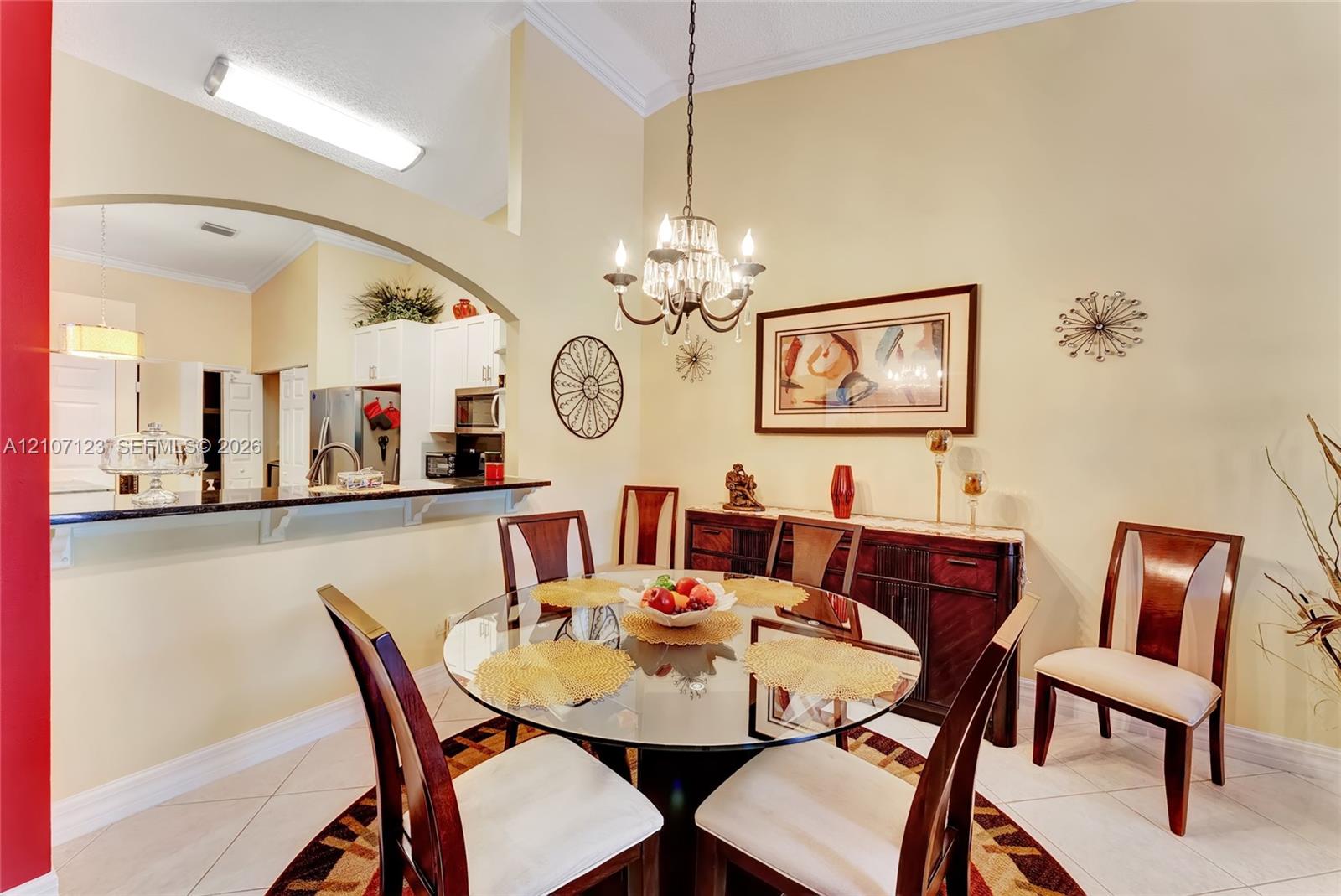 Dining area featuring vaulted ceilings, an arched wall opening, a decorative hanging chandelier, and neutral tile flooring