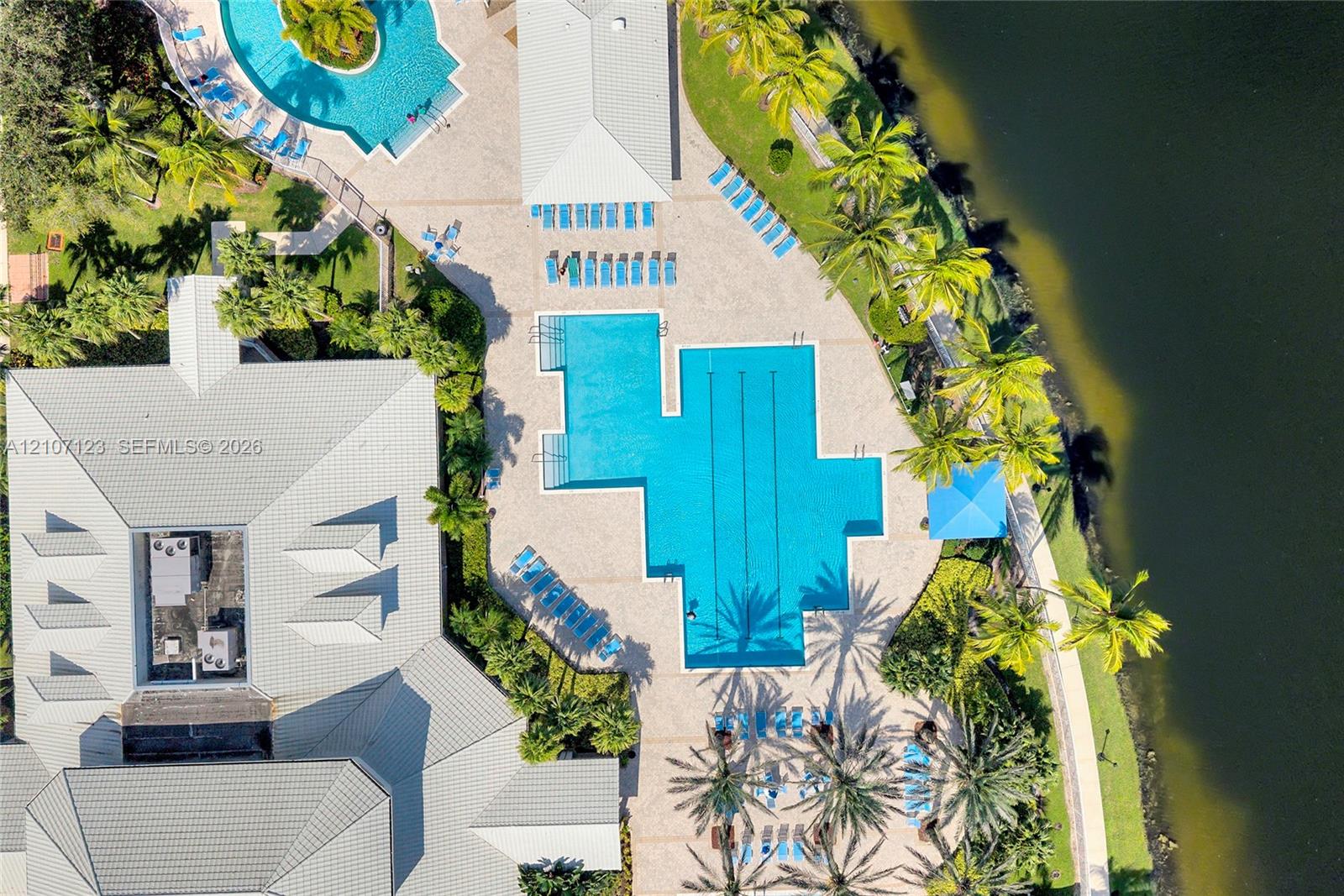Aerial perspective of a multi-level swimming pool, paved sundeck, covered structure, and water frontage