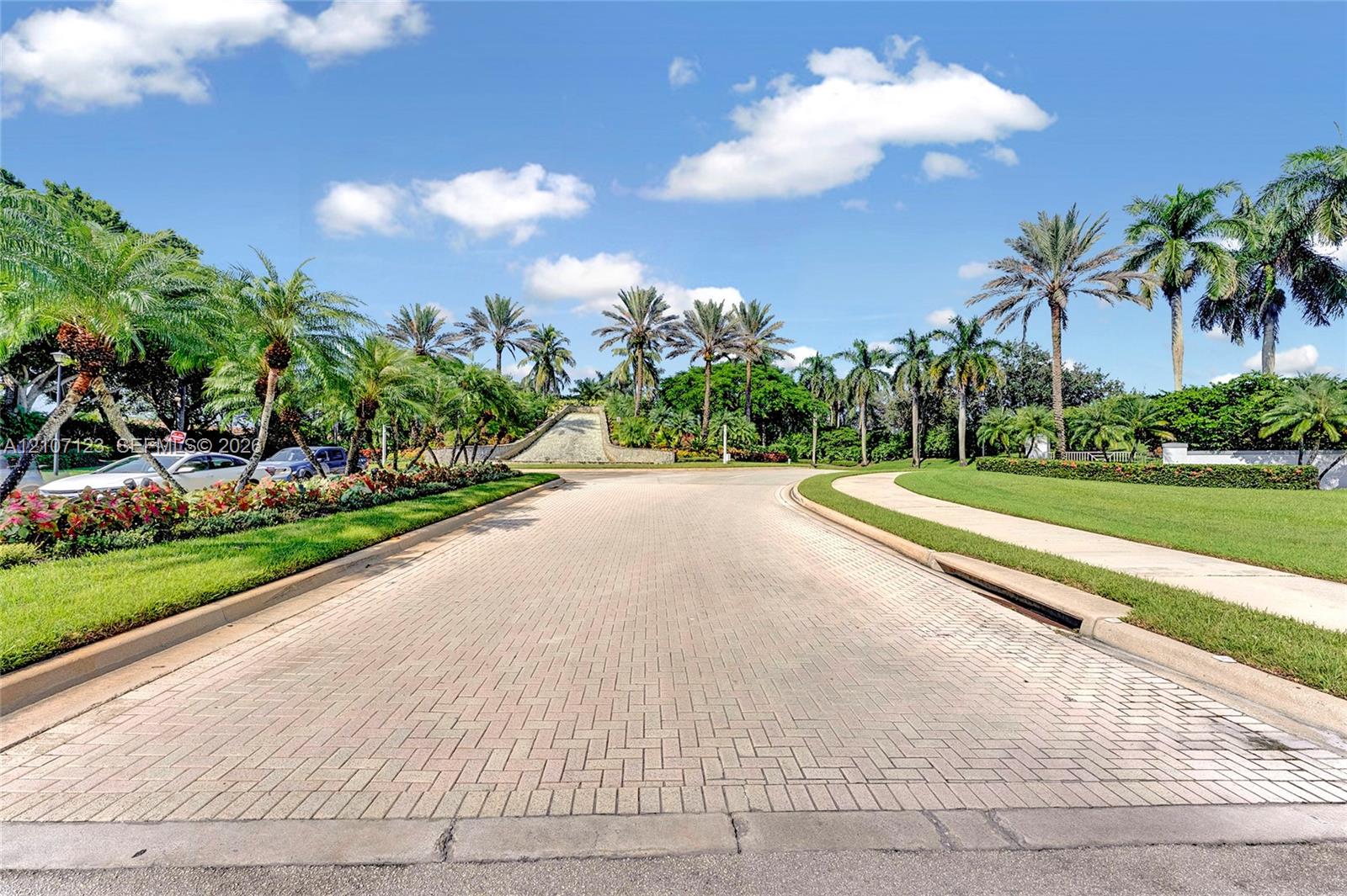 Paver stone entry road featuring mature palm trees, manicured turf, and extensive tropical landscaping