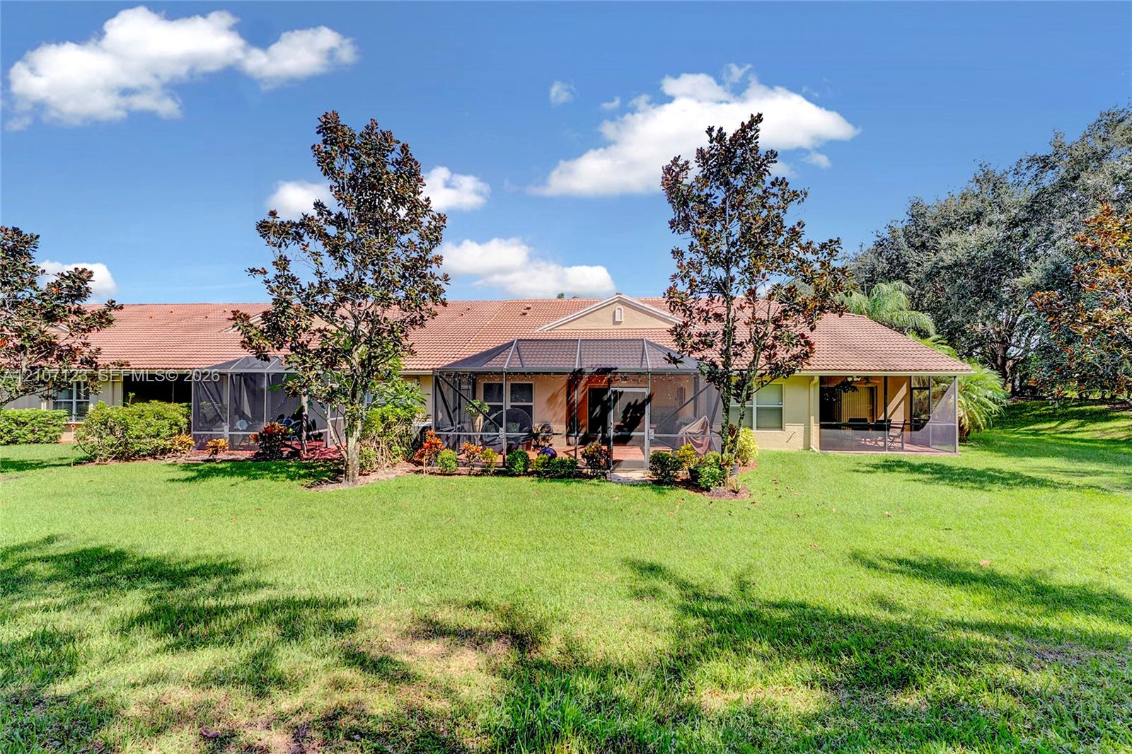 Expansive rear lawn featuring mature landscaping, multiple screened-in lanai enclosures, and a tiled roof