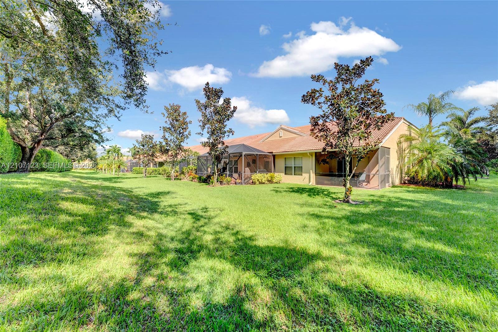 Expansive backyard featuring a manicured lawn, mature trees, and a screened-in rear patio