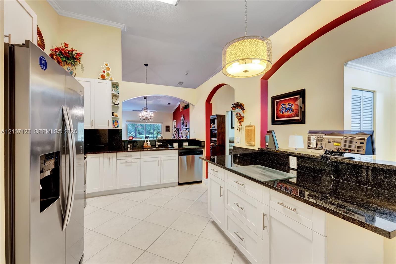 Kitchen featuring white shaker-style cabinetry, dark stone countertops, stainless steel appliances, tile flooring, and arched architectural detailing