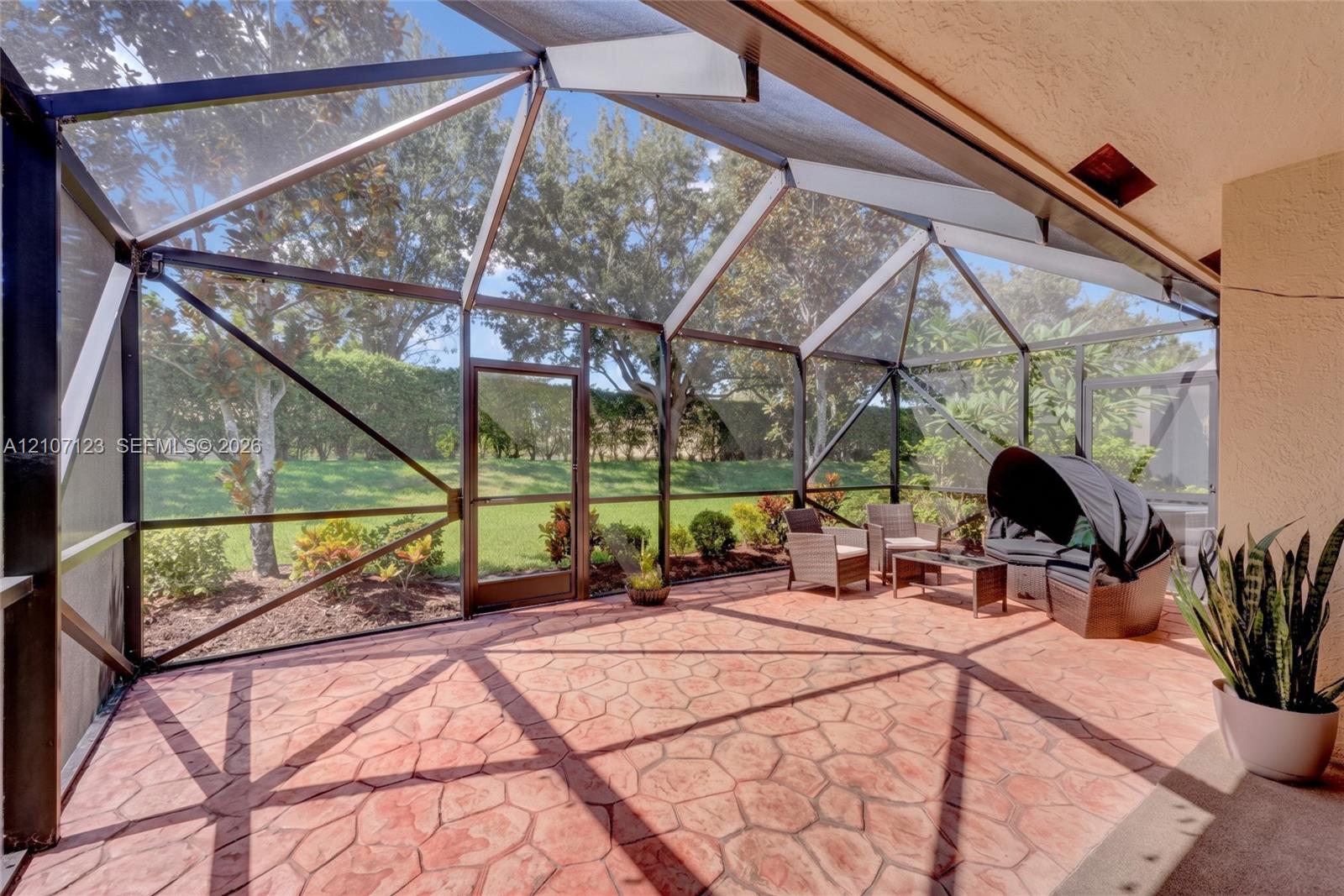 Screened-in patio featuring decorative stamped concrete flooring, dark metal framing, and a dedicated entry door