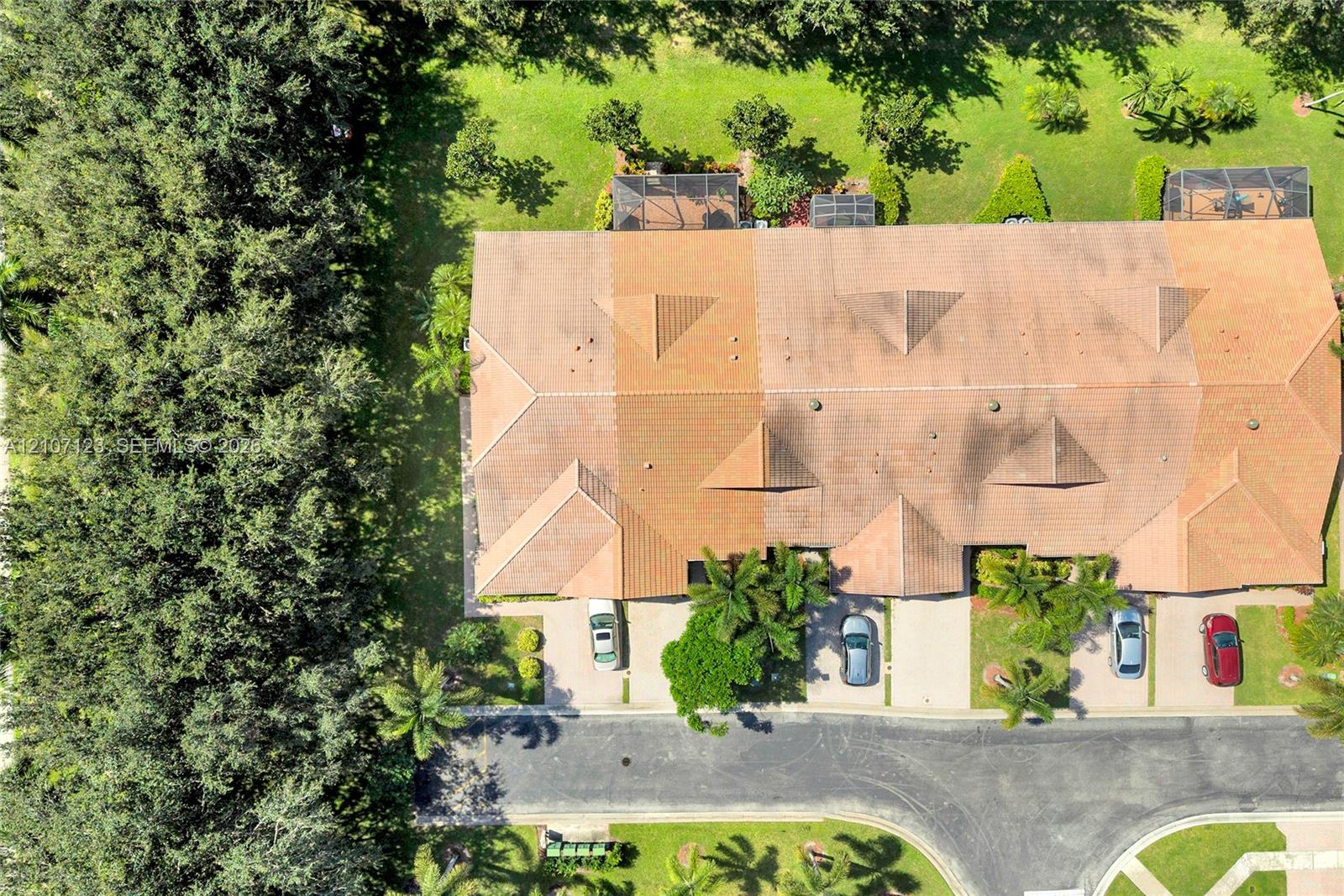 Aerial perspective of a multi-unit property featuring a multi-pitched tile roof, private screened-in patio areas, paved driveways, and surrounding mature landscaping