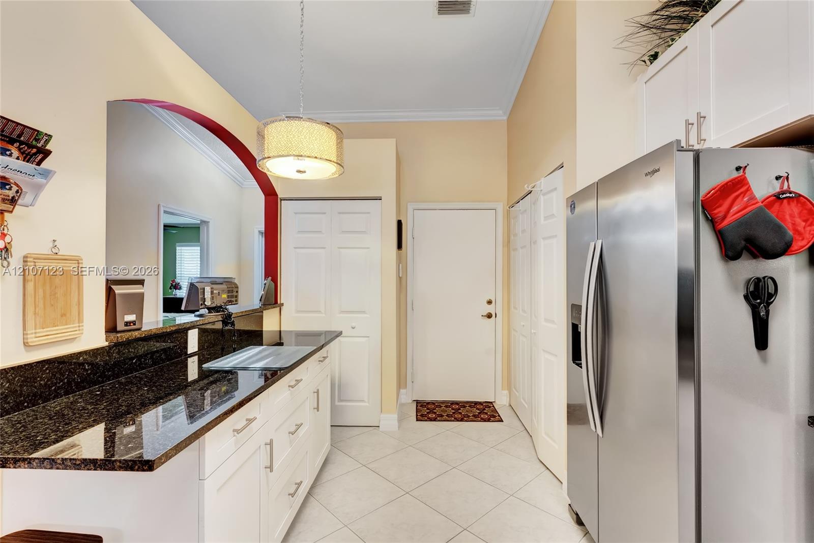 Kitchen featuring white cabinetry, dark stone-finish countertops, stainless steel side-by-side refrigerator, tile flooring, and a recessed archway accent