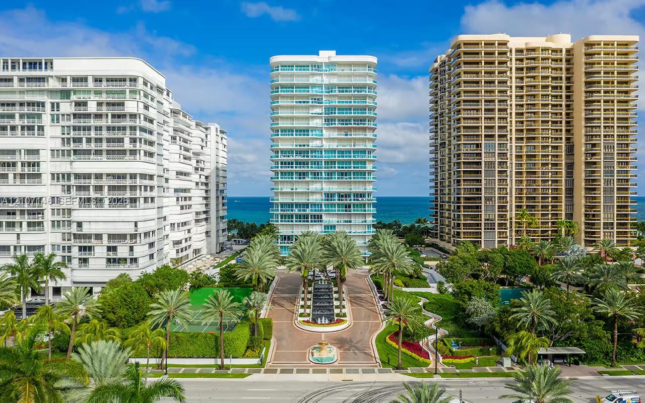 High-rise residential building with balcony glass railings, paved motor court with central fountain, private tennis court, and mature tropical landscaping