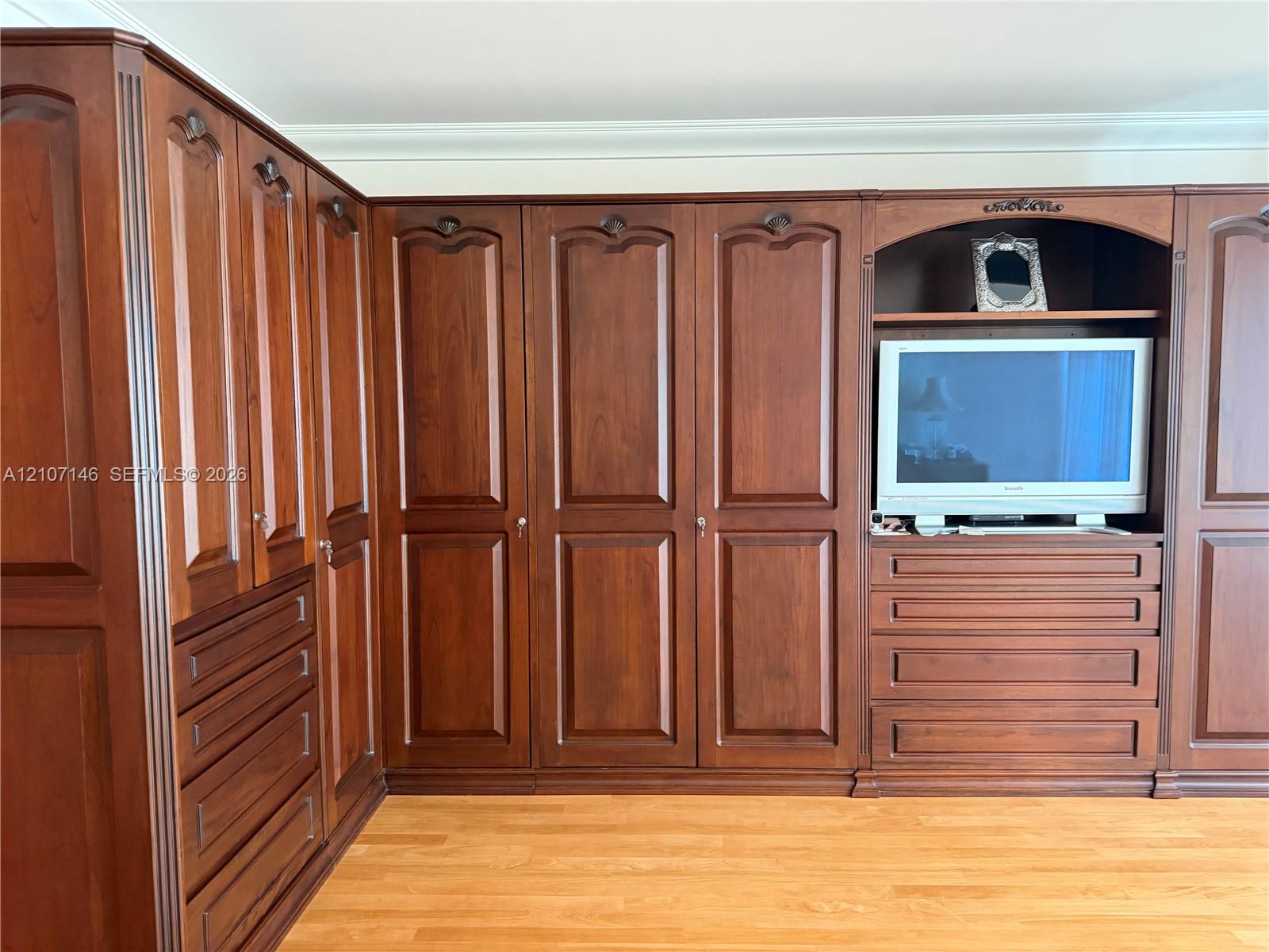 Wall-to-wall built-in cabinetry featuring rich-toned wood finish, raised-panel doors, integrated drawer banks, and crown molding accents, complemented by wood-finish flooring