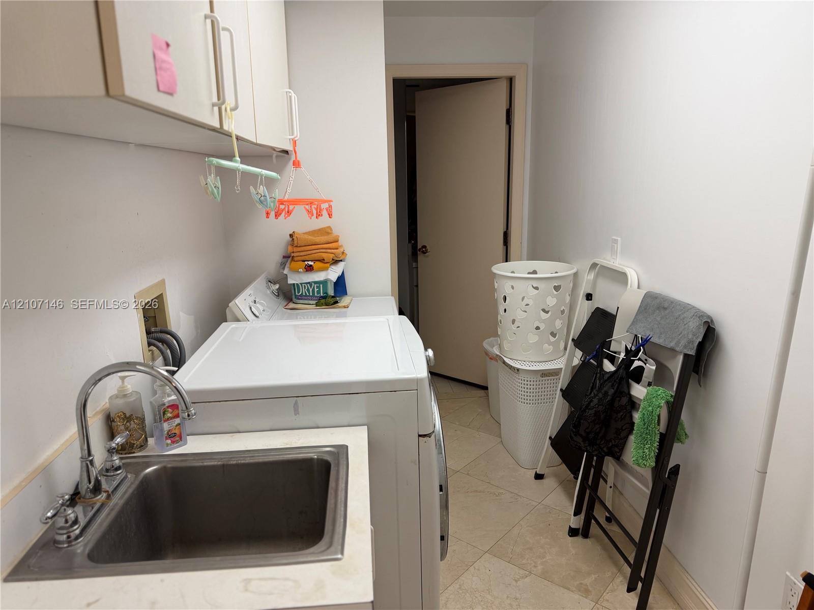 Laundry area featuring ceramic tile flooring, built-in cabinetry, and a drop-in stainless steel utility sink with a high-arch chrome faucet