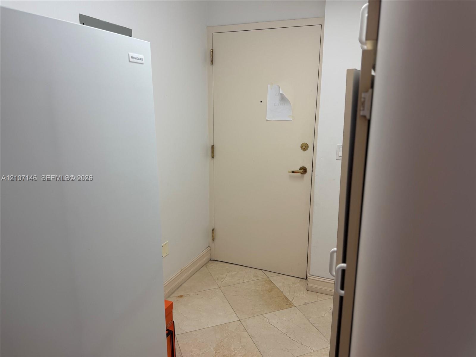 Neutral-toned tile flooring with an integrated, full-height white refrigerator and a solid-core entry door featuring brushed metal hardware