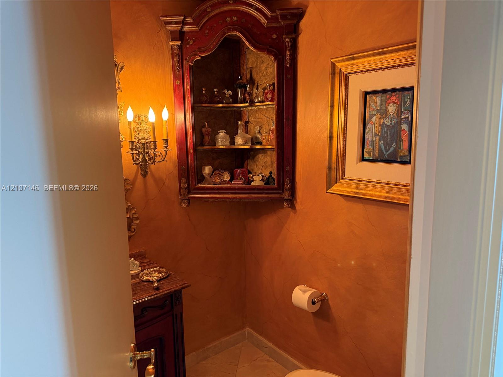 Custom built-in corner cabinet with ornate wood trim, Venetian plaster walls, intricate metal wall-mounted sconce, and tile flooring
